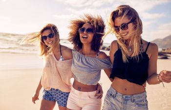 three young women friends walking along the beach