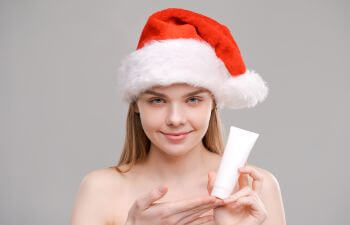 Beautiful woman in a Christmas hat holding a tub of skincare product.