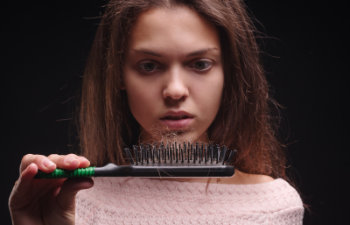 woman looks at a hair brush with ripped out damaged hair